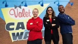 Group photo of diverse Valet Car Wash employees with our bulding signage in the background