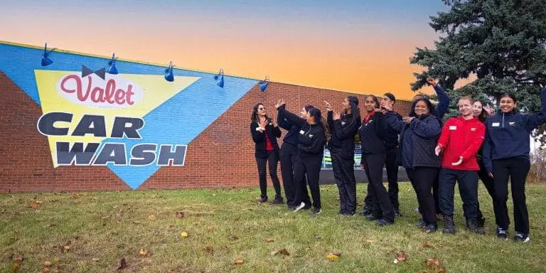 Picture of happy Valet employees next to a Valet Car Wash building, each pointing in every direction