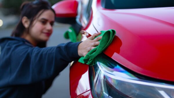 Woman using a green microfiber cloth to polish the hood of a red car