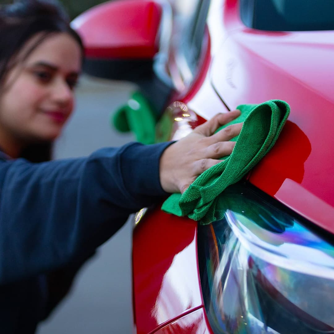 Woman using a green microfiber cloth to polish the hood of a red car