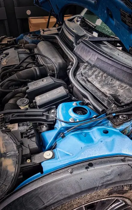 Close-up of a car engine bay with hood open, showing a blue-painted inner fender and various engine components