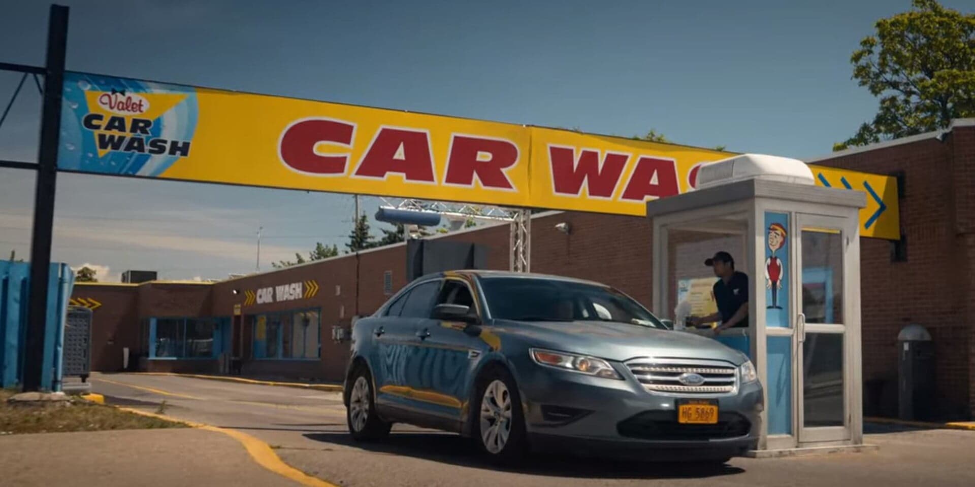 Scene from Netflix’s “Fubar” featuring Valet Car Wash, where a silver sedan pulls into the entrance of the wash, highlighting its role as a hidden tunnel to CIA headquarters in the show.