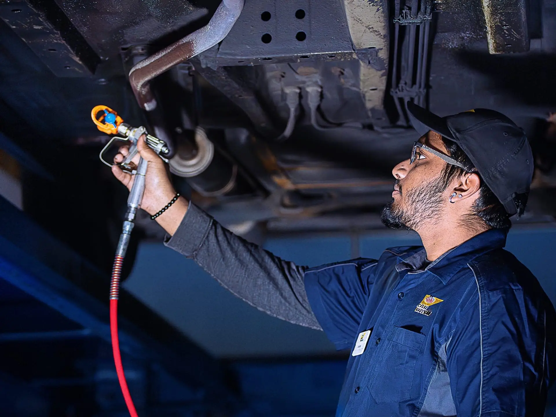 Valet technician spraying car underside with anti-rust oil