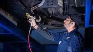 Valet technician spraying car underside with anti-rust oil