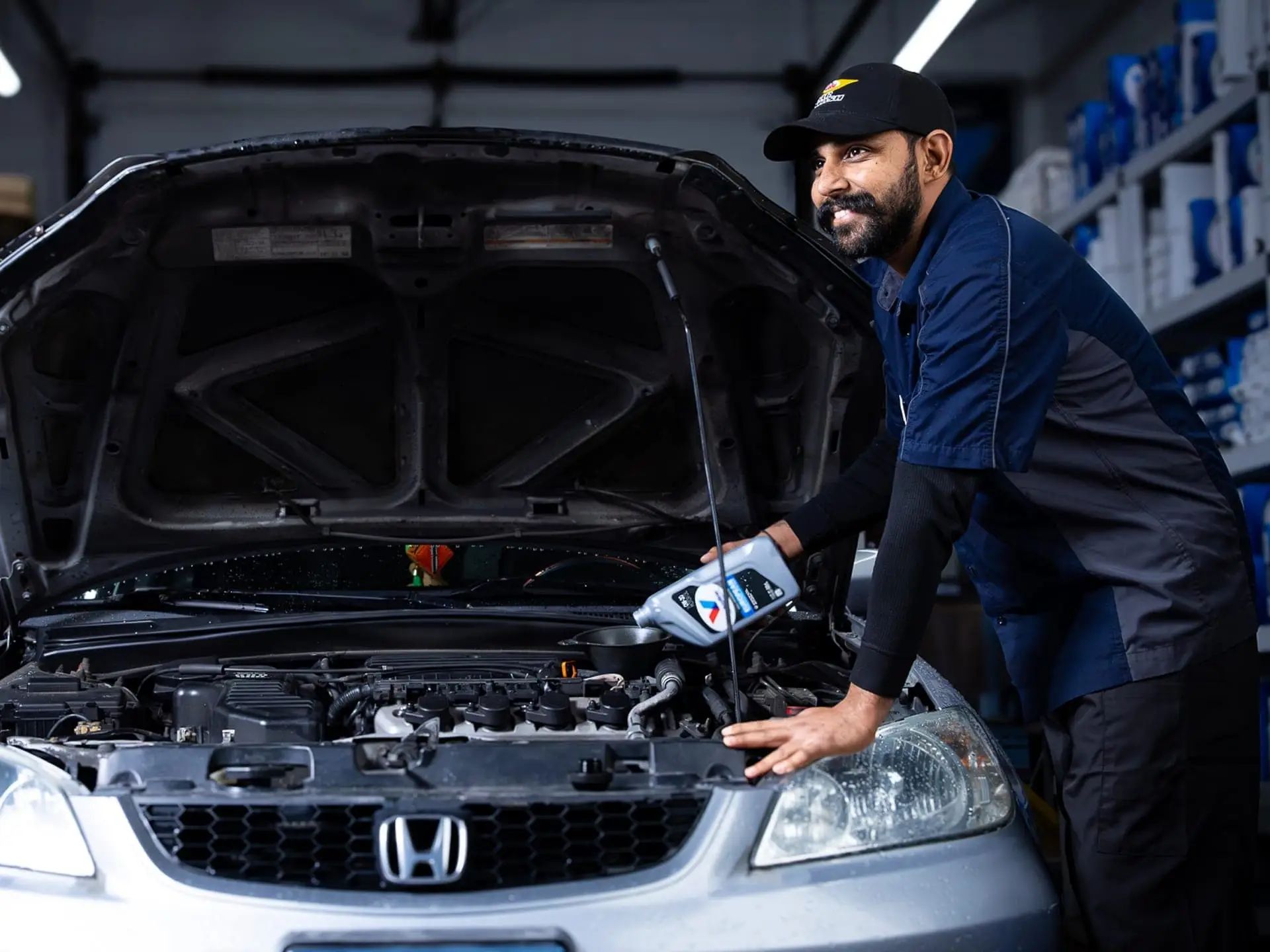 Valet technician patiently adding fresh oil to the engine of a customer's car