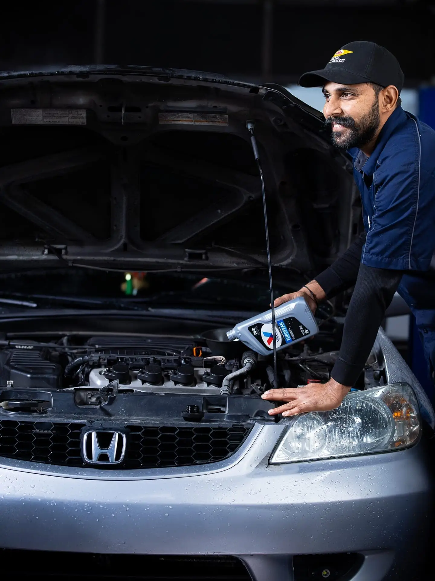 Valet technician patiently adding fresh oil to the engine of a customer's car