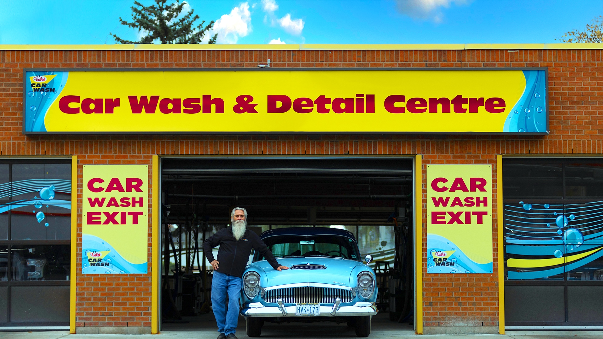 Person with a majestic beard leaning against their rare blue 1955 Kaiser Manhattan, at a Valet Car Wash & Detail Centre