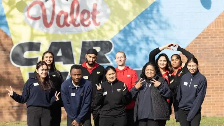 Group photo of diverse Valet Car Wash employees with our bulding signage in the background