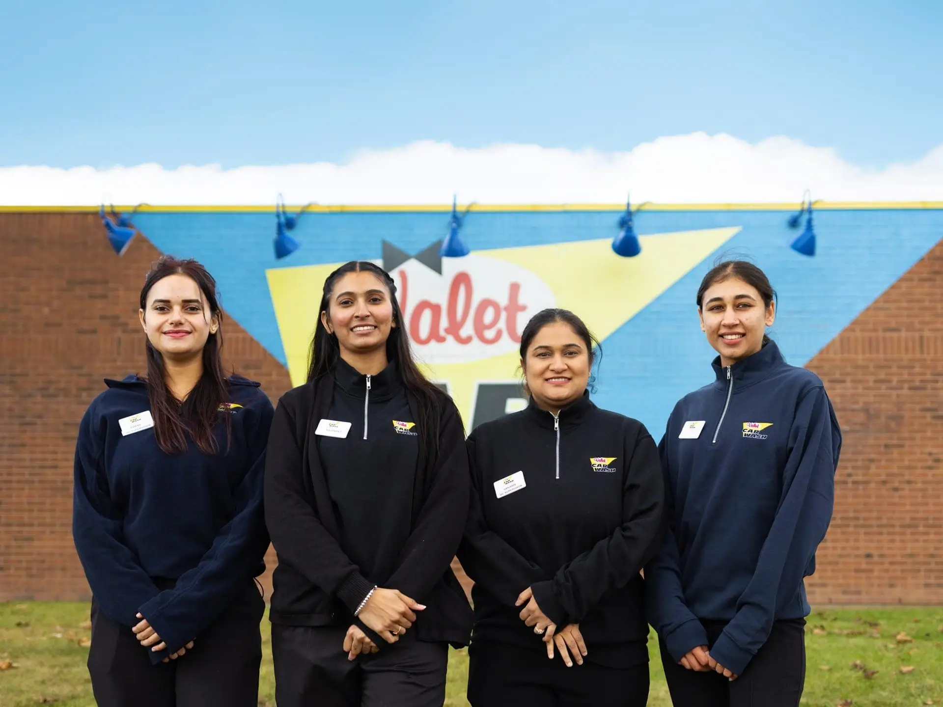 Group photo of diverse Valet Car Wash employees with our bulding signage in the background