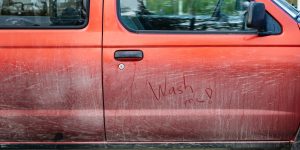 Picture of the side of a dirty orange car, with 'wash me!' written