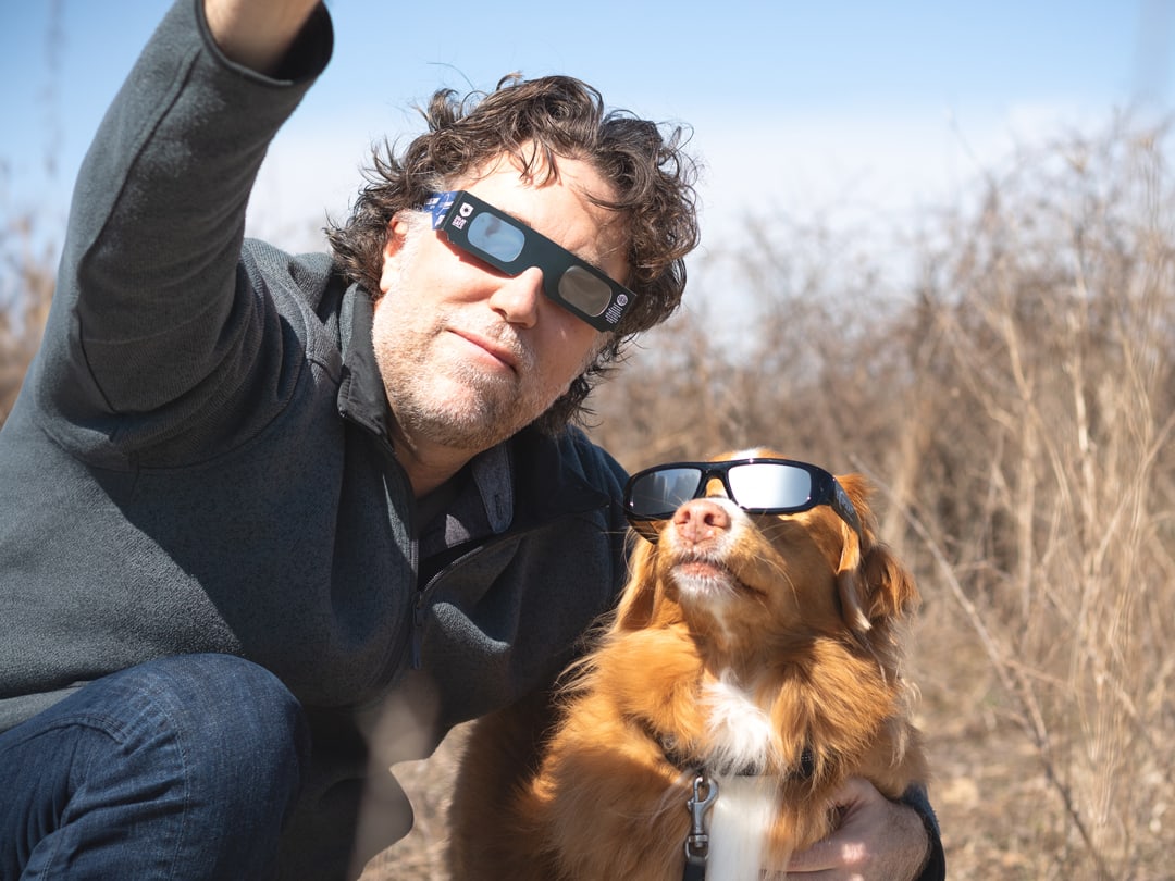 A person and their dog, both with proper eye protection, looking at a solar eclipse