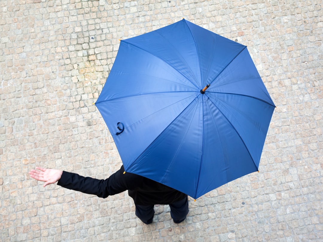 Picture of a person checking if it's raining with their hand from under their umbrella