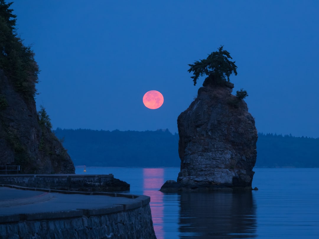 A landscape of the Siwash Rock with a full moon in the background