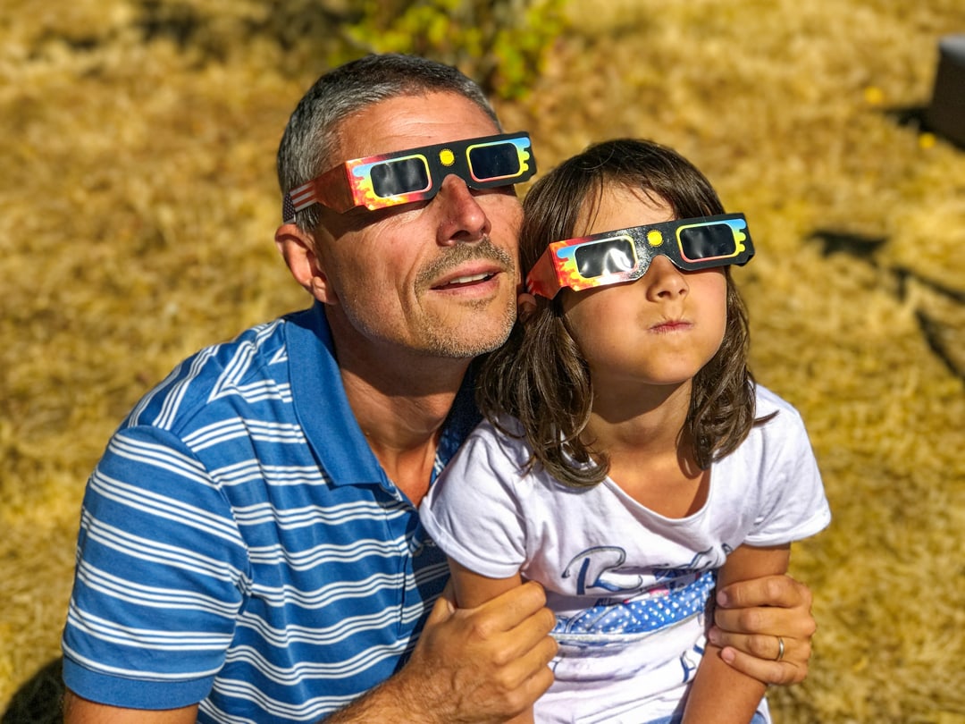 Picture of a kid and their dad looking at a solar eclipse using the proper eye protection