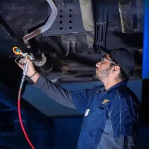 Valet technician applying No Drip Oil Spray Rust Protection to the underside of a vehicle, ensuring long-lasting protection against rust and corrosion in harsh conditions.