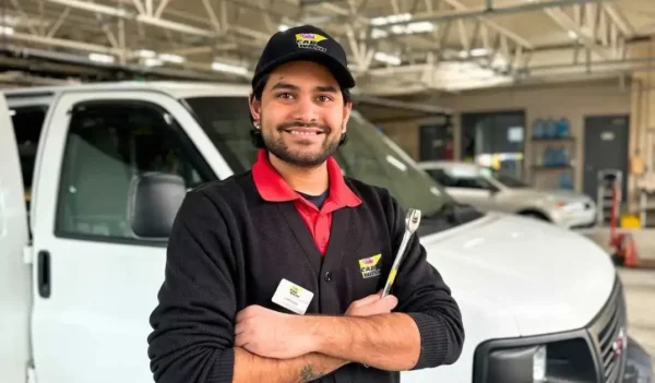 Smiling technician in Rightlook Car Wash uniform holding a wrench, standing in front of service vans in a garage