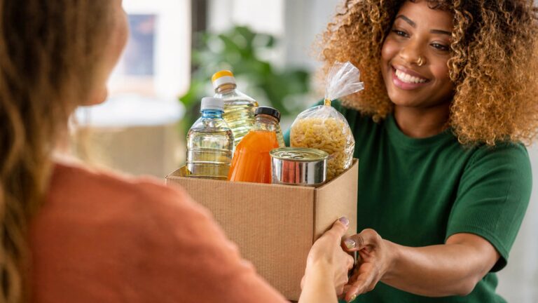 Smiling woman receiving a box of food staples including oil, pasta, and canned goods